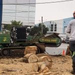 A worker is using a large machine to grind a tree stump, while wearing protective gear. The image demonstrates the process of grinding a tree stump.