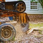 Tree root grinding machine in action removing roots near a home foundation in a leafy Australian backyard.